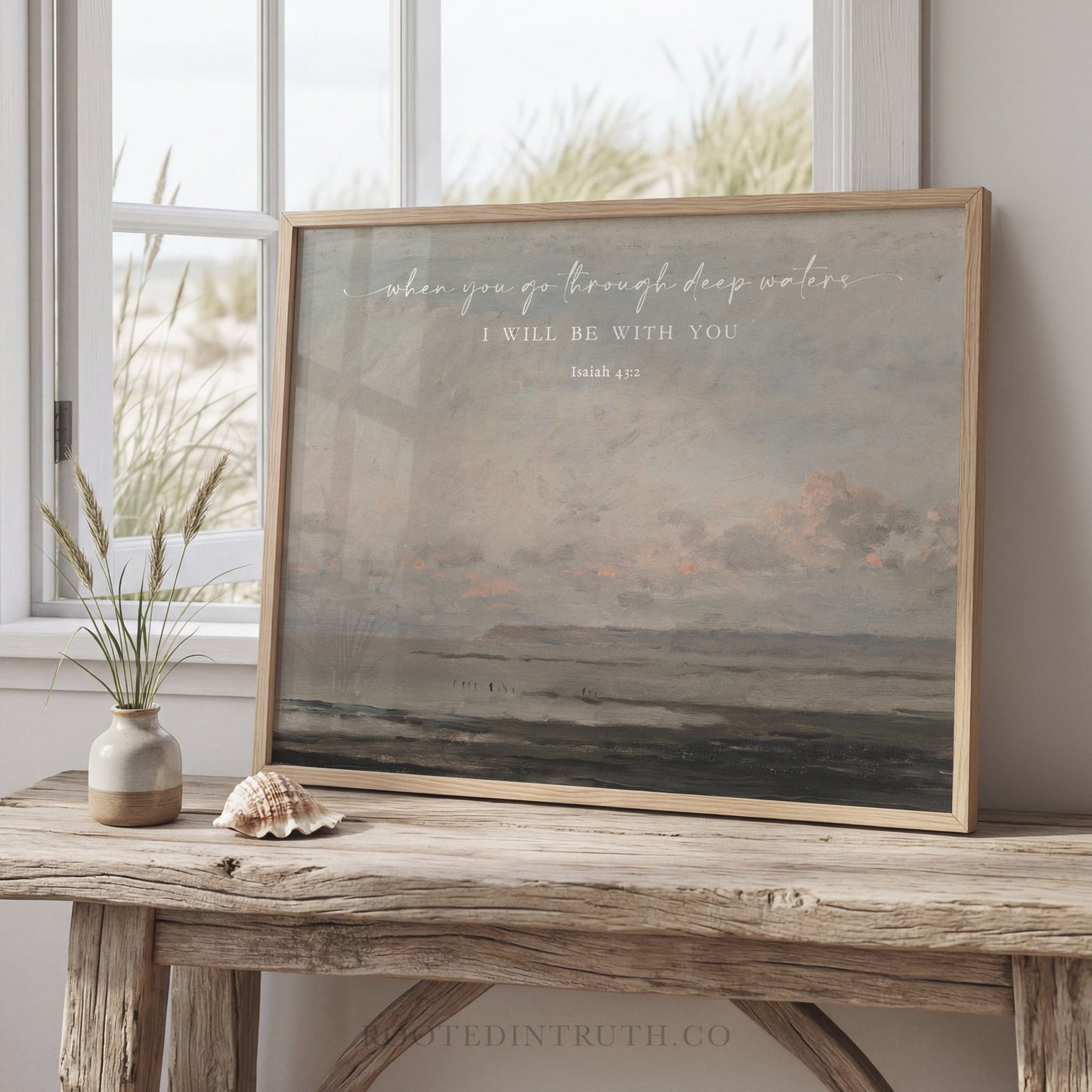 a framed painting of a serene landscape, with a vase of flowers and a seashell on a wooden table in front of it.