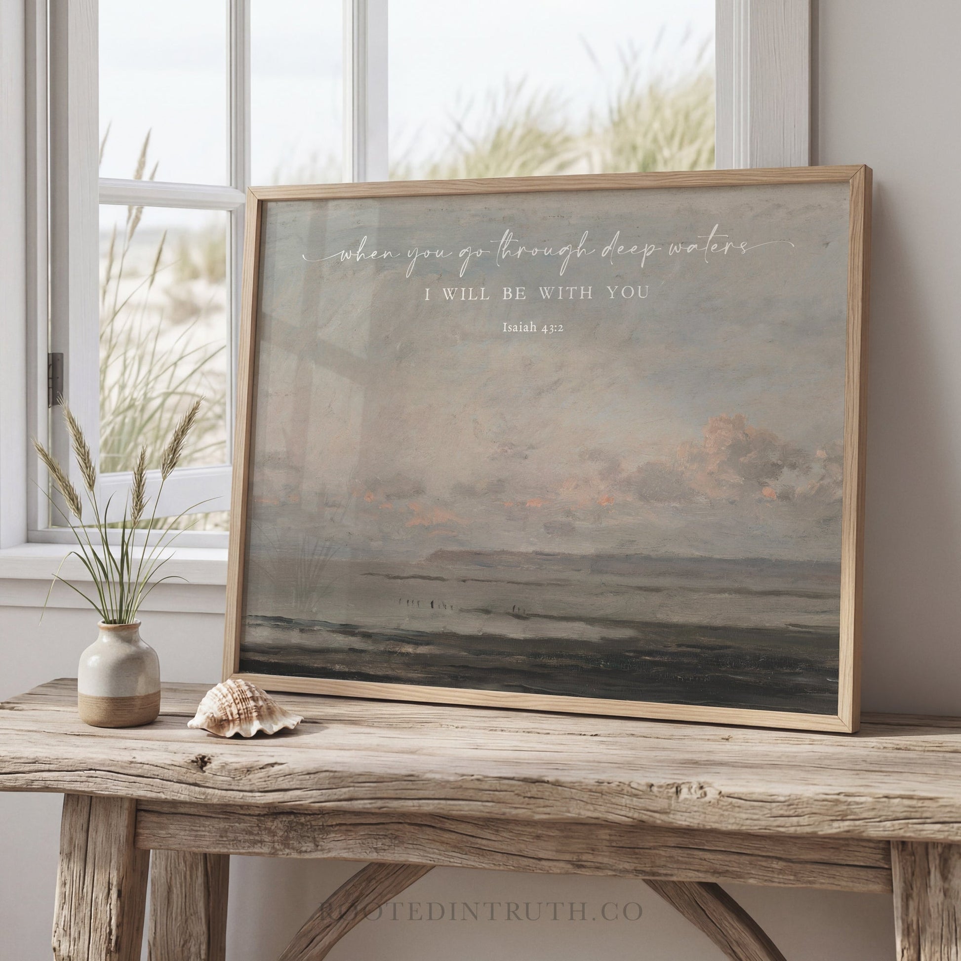 a framed painting of a serene landscape, with a vase of flowers and a seashell on a wooden table in front of it.
