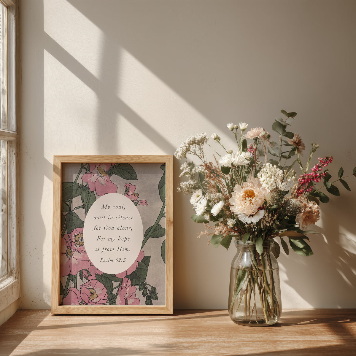 a wooden table with a framed print of a floral design next to a glass vase filled with a bouquet of flowers. The print includes a Bible verse from Psalm 52:5.
