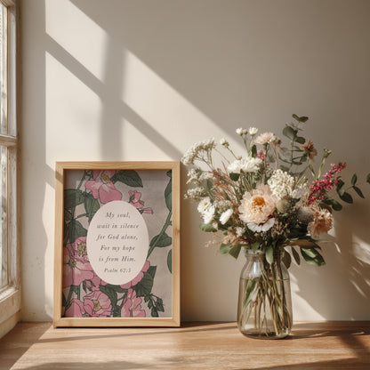a wooden table with a framed print of a floral design next to a glass vase filled with a bouquet of flowers. The print includes a Bible verse from Psalm 52:5.