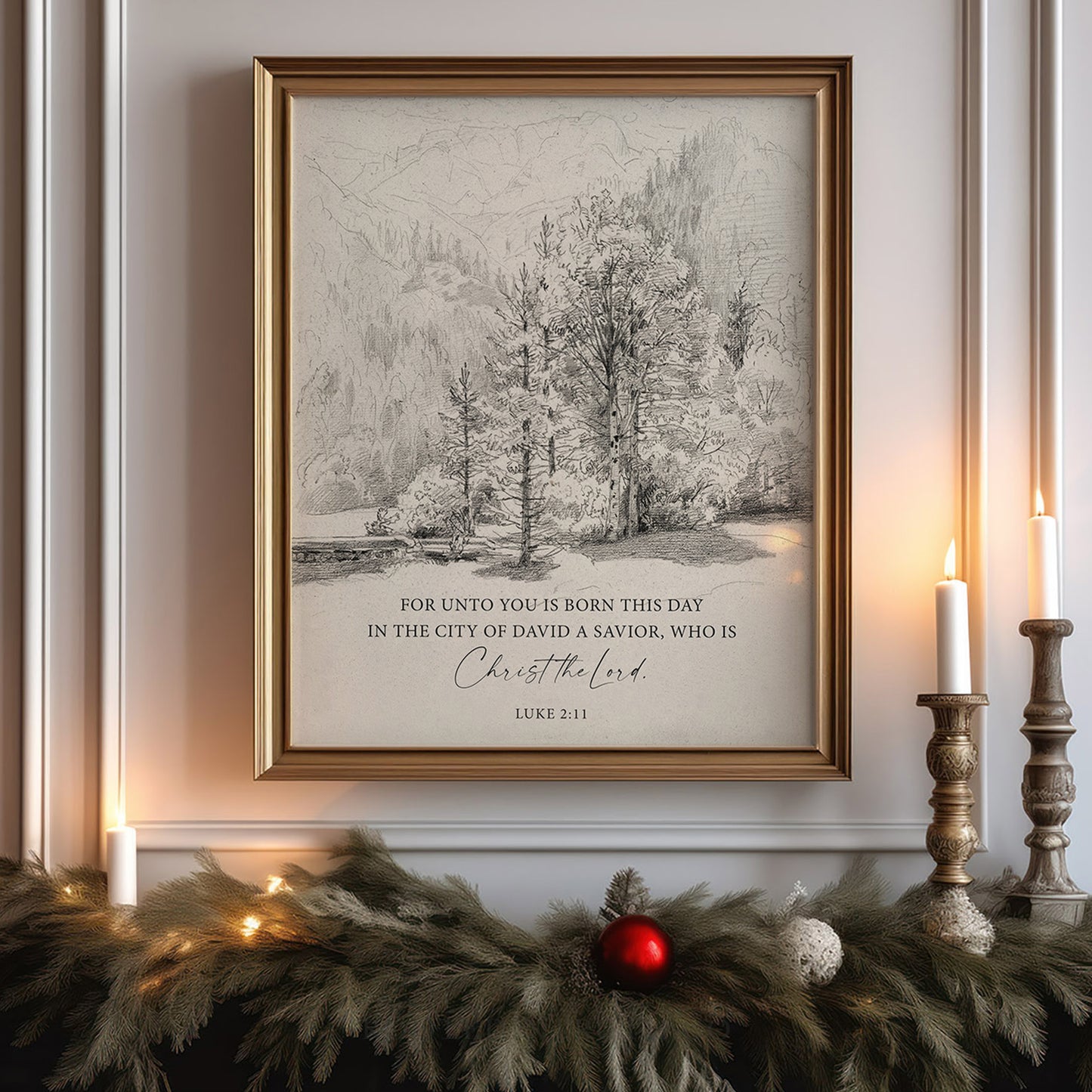 a framed print of a winter landscape with a Bible verse from Luke 2:11, which reads "For unto you is born this day in the city of david a Savior, who is Christ the Lord". The print is displayed on a wall, and there are candles and greenery, such as pine branches, arranged in front of it.