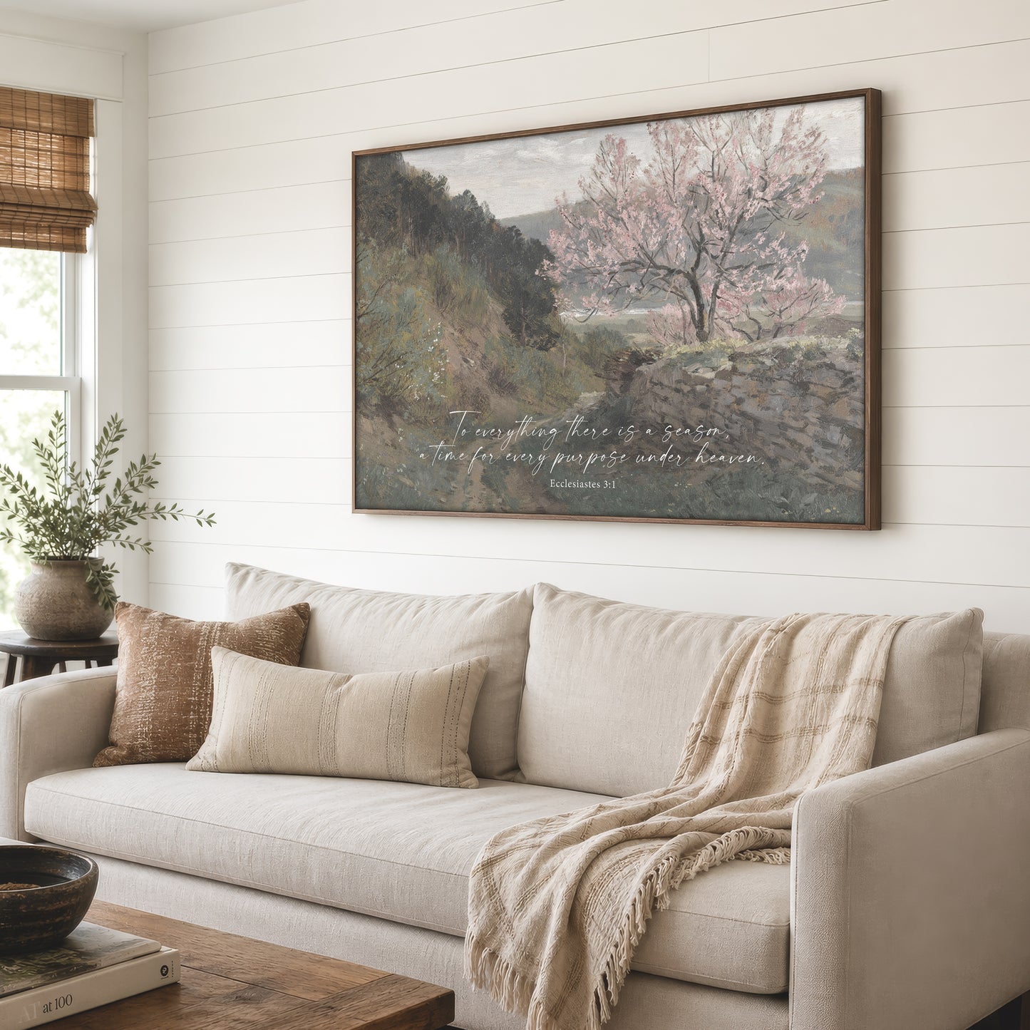 a large painting of a tree with pink blossoms hanging on a wall above a beige sofa with throw pillows.