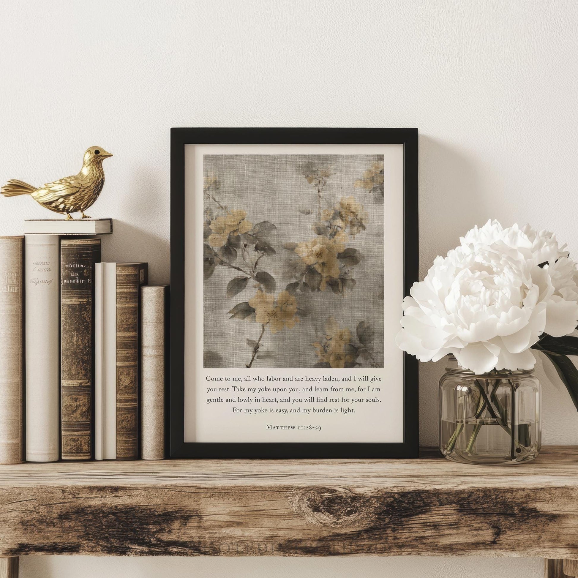 A framed print of a floral painting is displayed on a wooden shelf, accompanied by a vase of white flowers and a small golden bird figurine.