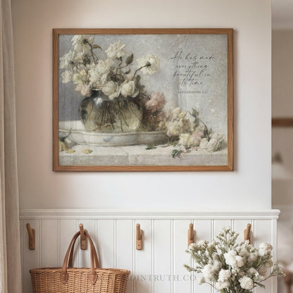 a framed painting of a vase filled with white flowers, hanging on a wall above a wooden shelf with a wicker basket.