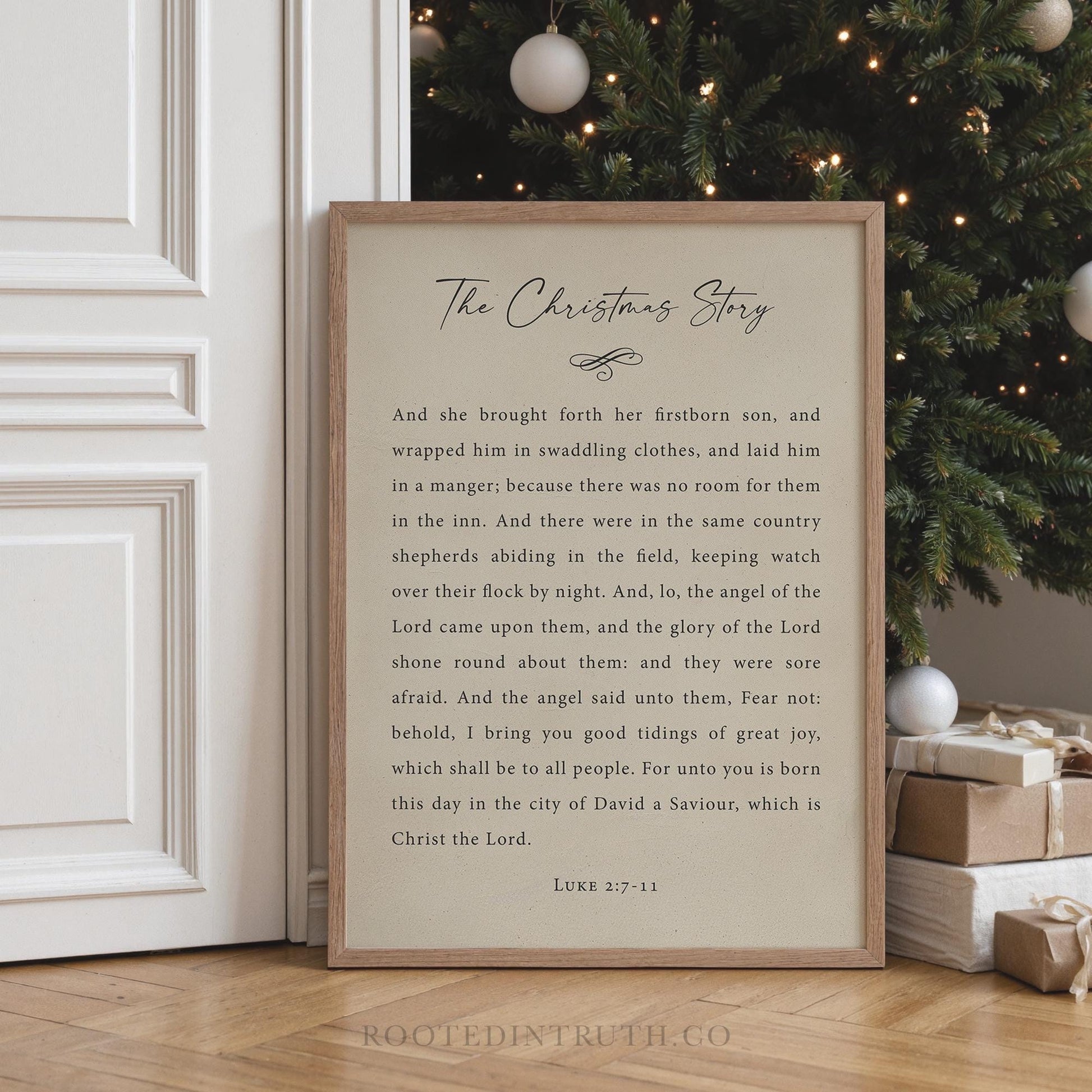 a framed text titled "The Christmas Story" with a Bible verse from Luke 17:11, which is a passage from the book of Luke. The text is written in a cursive font and is displayed on a white door. In the background, there is a Christmas tree and some wrapped gifts, creating a festive atmosphere.