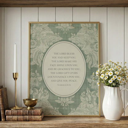 a framed print with a religious text, a white vase with white flowers, a stack of books, and a brass candlestick on a wooden shelf.