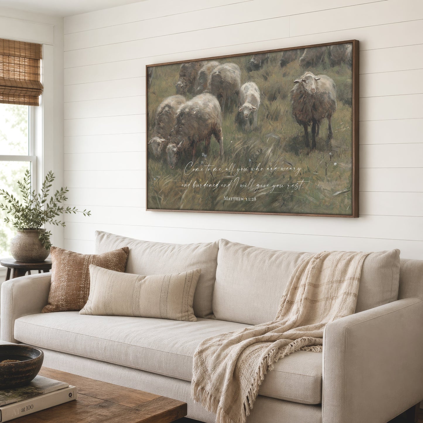 a large painting of a pastoral scene with sheep grazing in a grassy field, hanging on a wall above a beige sofa in a cozy living room setting.