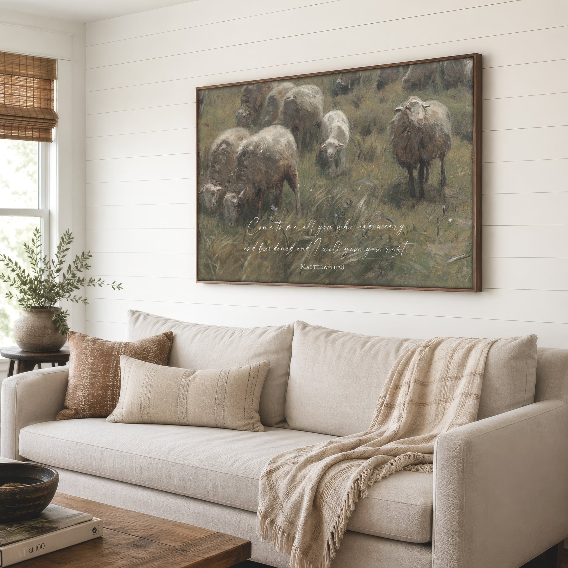 a large painting of a pastoral scene with sheep grazing in a grassy field, hanging on a wall above a beige sofa in a cozy living room setting.