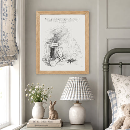 a bedroom scene with a framed illustration of a bear sitting in a log cabin, a lamp, a vase with flowers, and a teddy bear on a bed.
