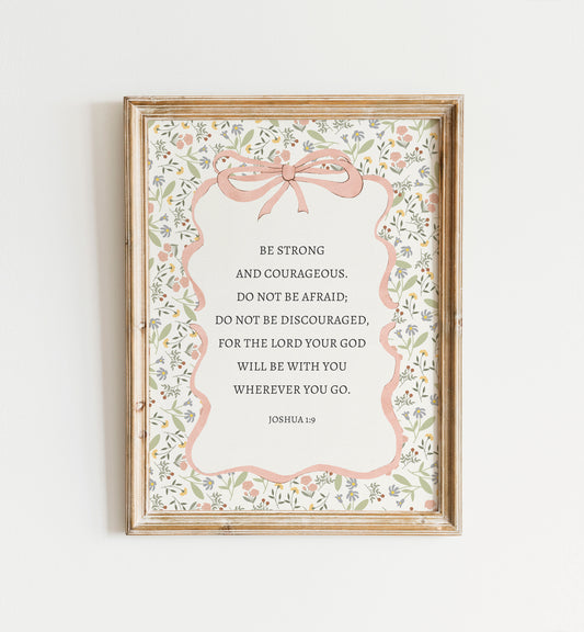 The image is a framed print with a floral border and a pink ribbon bow. The print contains a Bible verse from Joshua 1:9, which encourages being strong and Courageous, not being afraid, and not being discouraged.