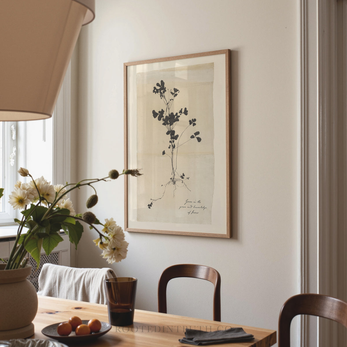 a dining room with a wooden table, two chairs, a vase with flowers, and a framed print hanging on the wall.