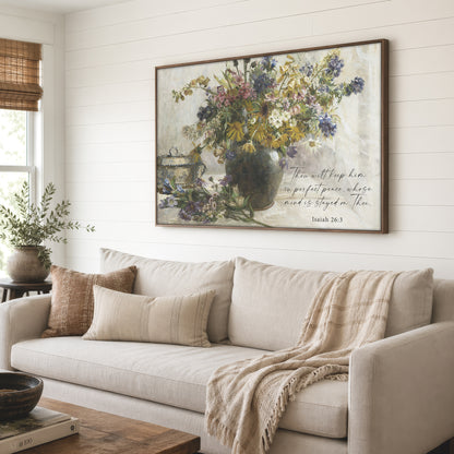 a large framed painting of a vase filled with flowers, hanging on a wall above a beige sofa with a throw blanket draped over it.