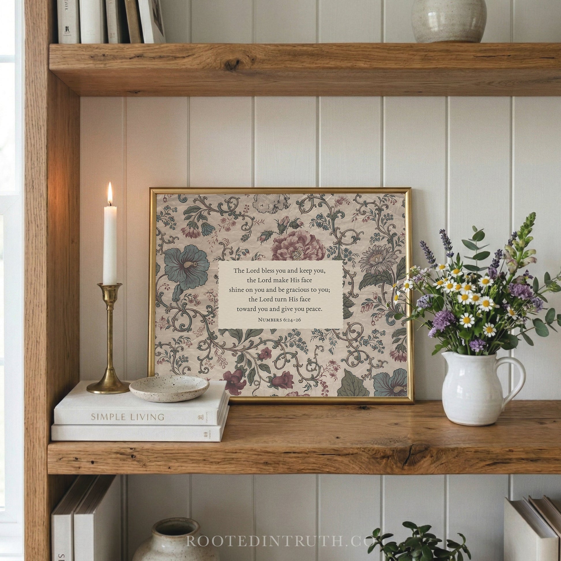 a wooden bookshelf with a framed print of a floral design, a white candle, a white vase with flowers, and a stack of books.