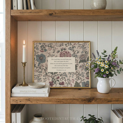 a wooden bookshelf with a framed print of a floral design, a white candle, a white vase with flowers, and a stack of books.