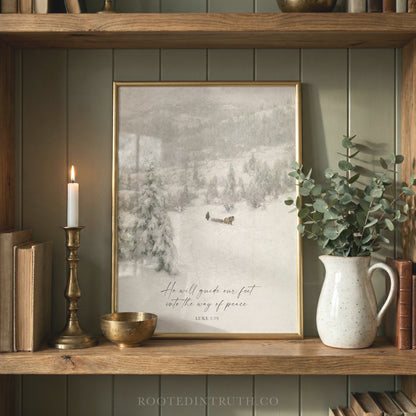 A framed print of a snowy landscape with a quote from Luke 15:1-2 is displayed on a wooden shelf, accompanied by a lit candle, a white vase with greenery, and a small bowl.