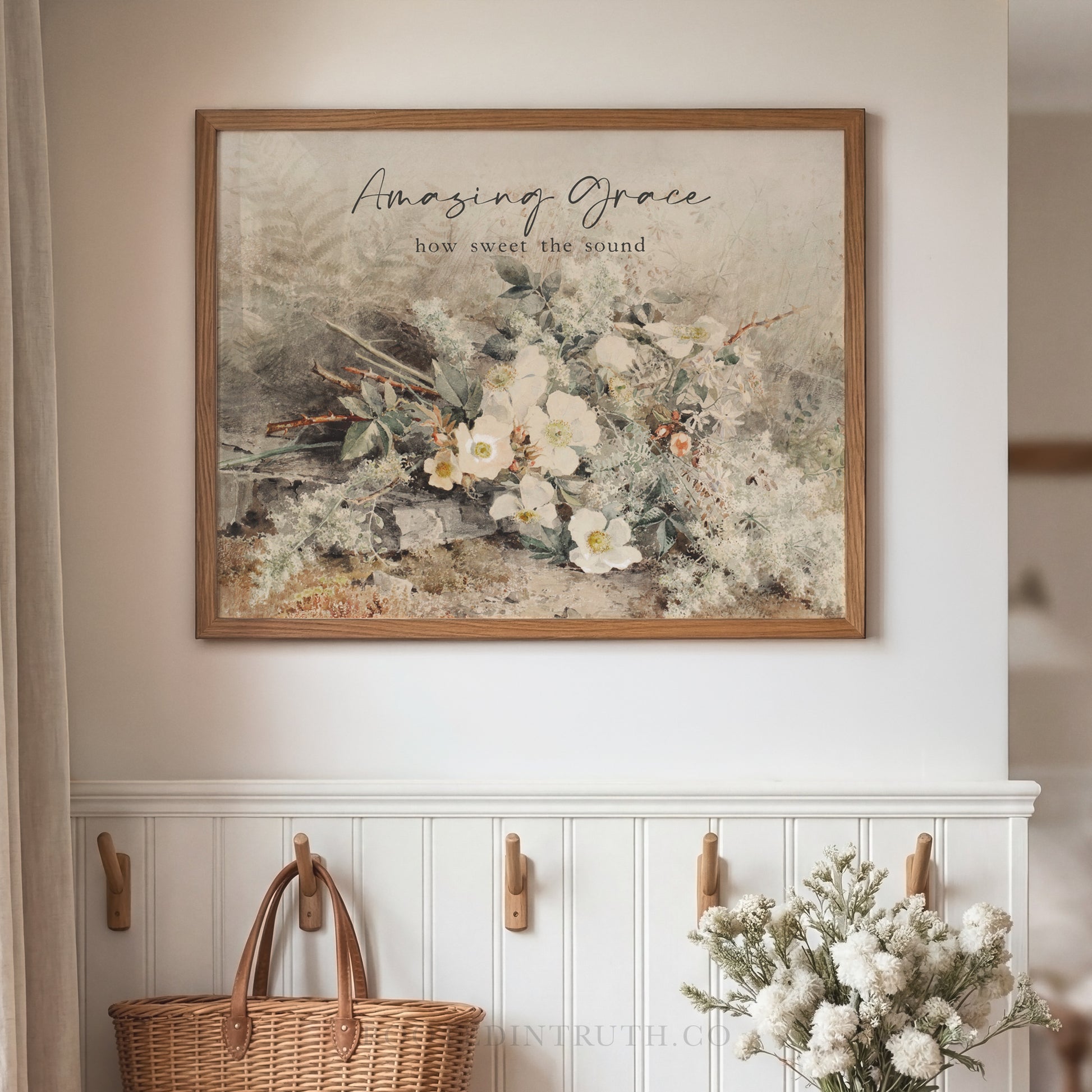 a framed print of a floral arrangement hanging on a wall, with a wicker basket and a vase of white flowers placed below it.
