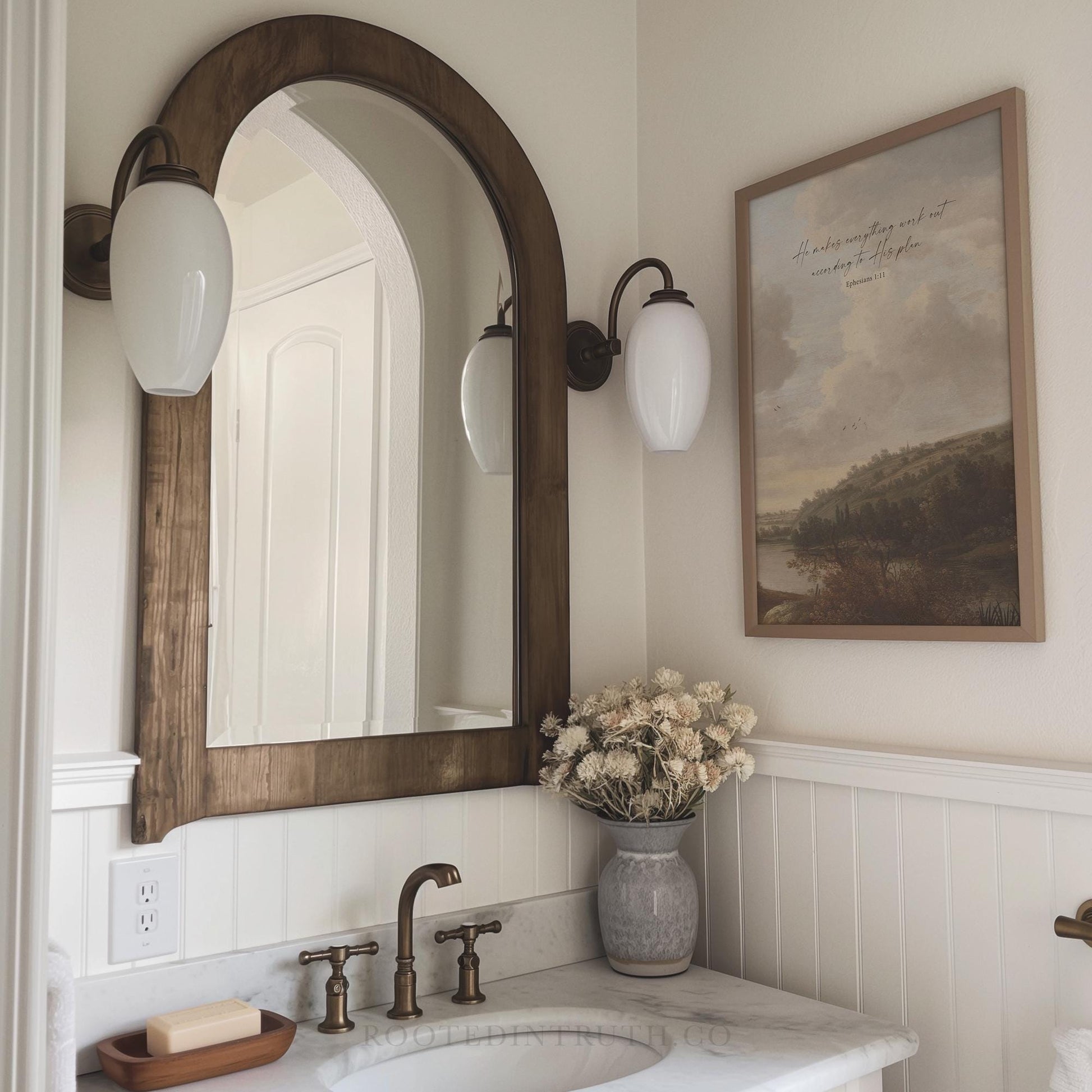 A Christian vintage wall art print with a scripture bible verse. Moody landscape in a bathroom with a sink and a mirror.