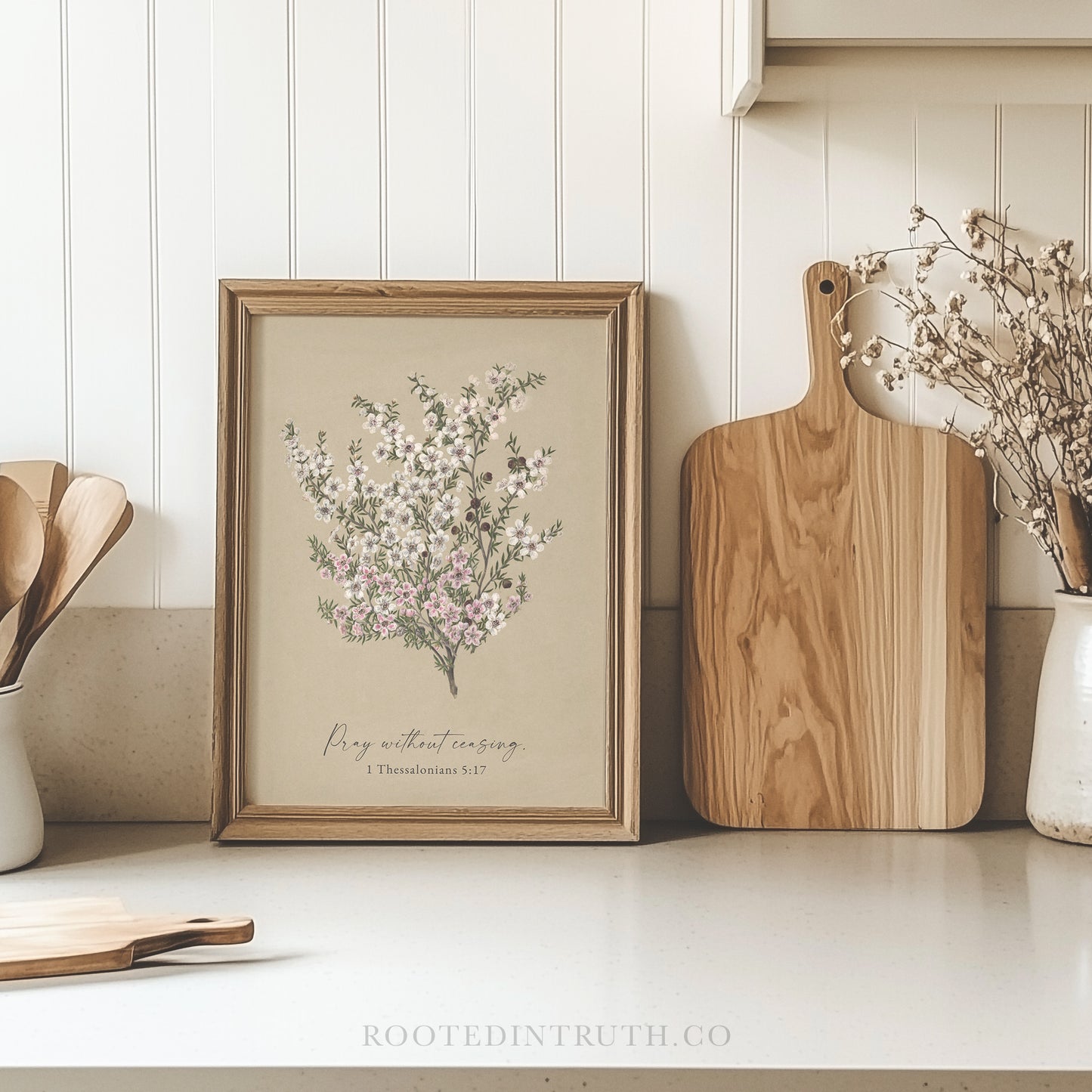 a framed print of a floral arrangement on a kitchen counter, accompanied by wooden cutting boards and a vase of dried flowers.
