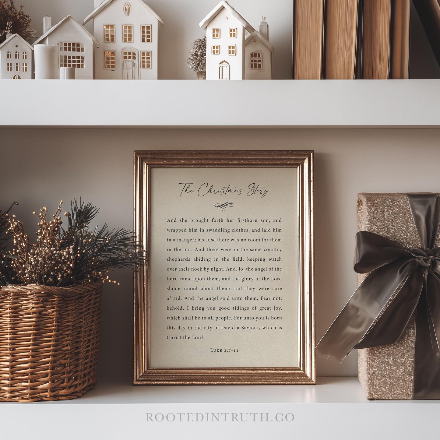 a framed Christmas-themed text on a shelf, with a wicker basket of greenery and a gift box with a bow to the right.