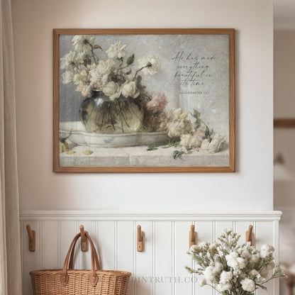 a framed painting of a vase filled with white flowers, hanging on a wall above a wooden shelf with a wicker basket.