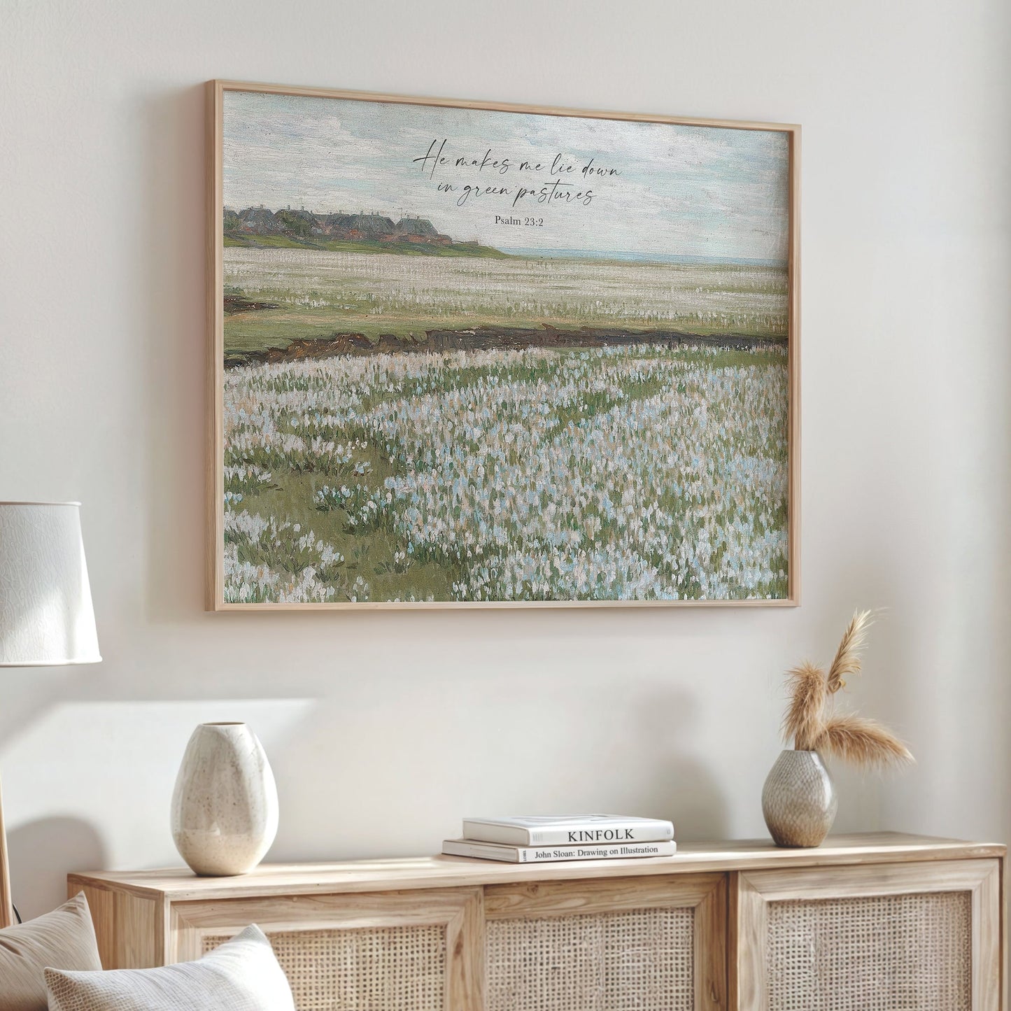 a large framed painting of a field with tall grass, hanging on a wall above a wooden cabinet with decorative items on top.